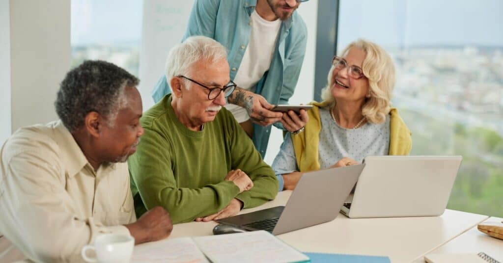 A small group of multicultural senior people are reading on their laptops about why charities need good systems.