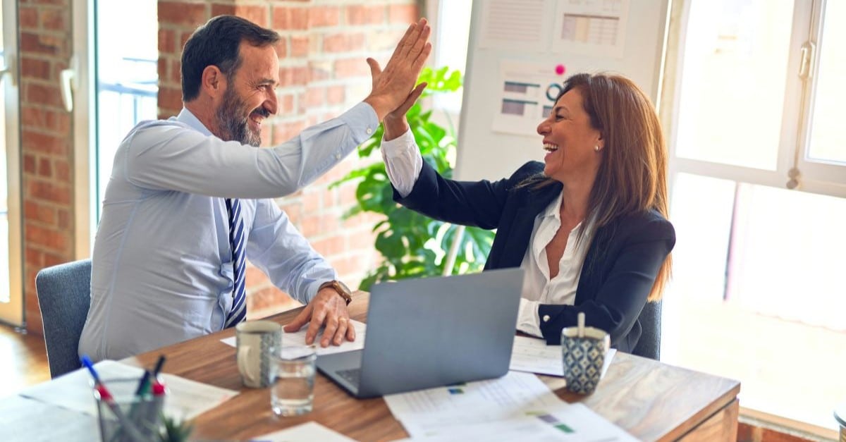 Two people working together at their computer and high fiving each other as they have just read about how to save time with their data entry.