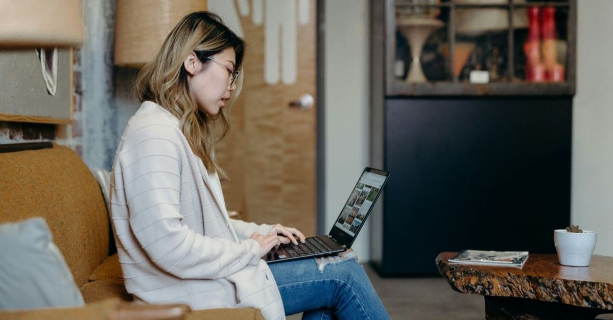 Woman sitting with her laptop on a sofa, reading up on how to choose a charity CRM.