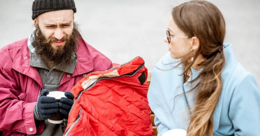 Homeless person with a woman listening to his story while sitting together on the bench outdoors. Concept of human understanding